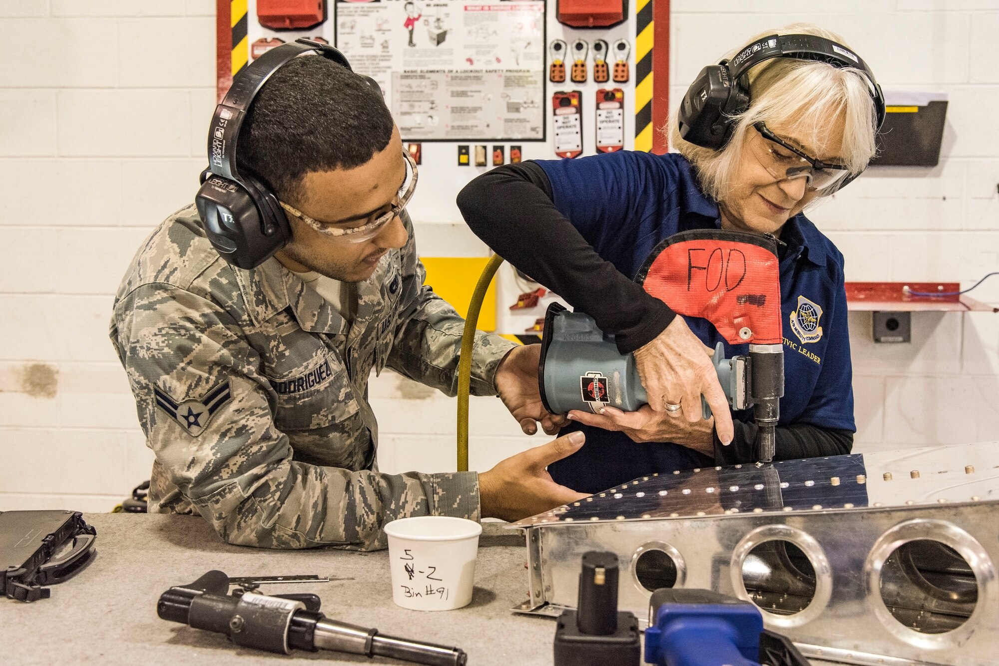 Airman 1st Class Reynaldo Rodriguez, 436th Maintenance Squadron aircraft structural maintenance journeyman, watches Yvonne Batts, Air Mobility Command civic leader from Dyess Air Force Base, Texas, install a rivet on a simulated aircraft part Nov. 7, 2018, at Dover Air Force Base, Del. Batts installed the rivet during her tour of the Fabrication Flight. (U.S. Air Force photo by Roland Balik)