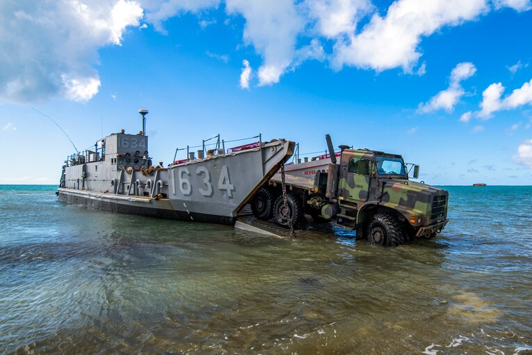 Soldiers drive an Army tactical vehicle off a Navy landing craft on a beach.