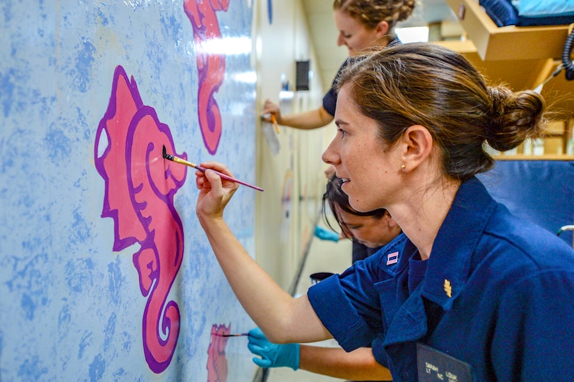 Sailors paint a mural on a wall.