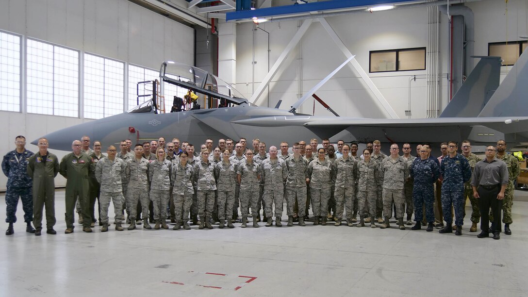 More than 50 service members stand in front of an F-15 on the factory floor.