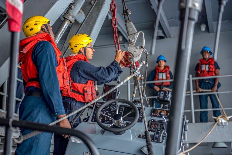 Two sailors secure chains with large hooks.