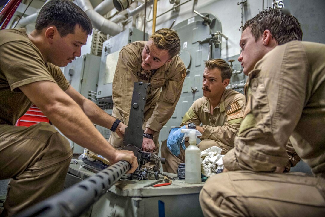 A sailor demonstrates gun maintenance for other sailors.