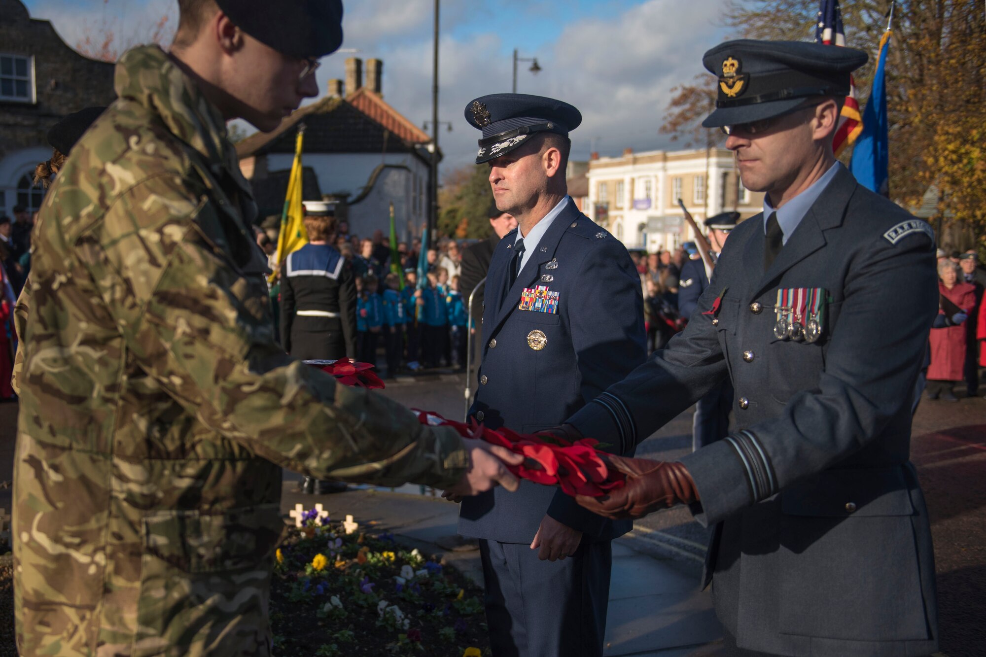 U.S. Air Force Lt. Col. Ryan White, 100th Maintenance Group deputy group commander and Royal Air Force Sqd. Ldr. Paul Graham, RAF Mildenhall station commander pass a poppy wreath to be placed on the war memorial during Remembrance Day in Mildenhall, England, Nov. 11, 2018. White and Graham presented the town with a poppy wreath in remembrance of World War I on behalf of Team Mildenhall Airmen and civilian personnel. (U.S. Air Force photo by Staff Sgt. Christine Groening)