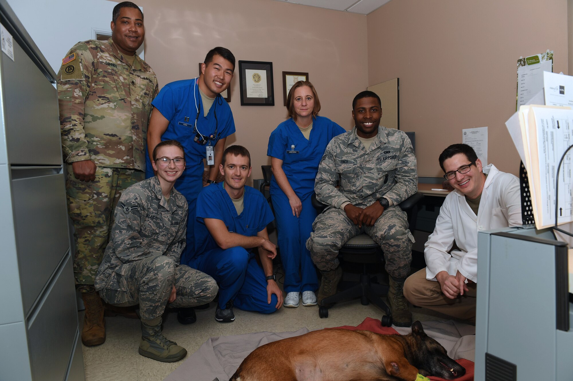 A group of people pose behind a dog sleeping on the floor.