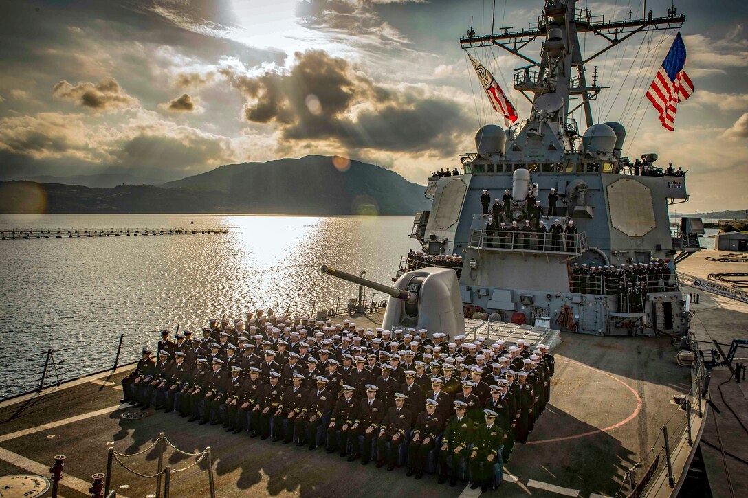 Sailors stand in formation on the deck of a ship for a photo.
