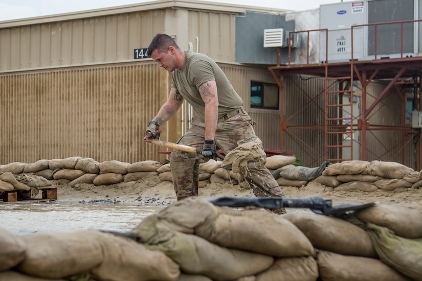 U.S. Army Sgt. Andrew Garden, a wheeled vehicle mechanic assigned to the 949th Veterinary Services Detachment, 8th Medical Brigade, carries a shovelful of sand while reinforcing barriers built to divert flood waters at Camp Arifjan, Kuwait, November 15, 2018. Soldiers from multiple units joined together to respond to the flooding which had impacted their living quarters.