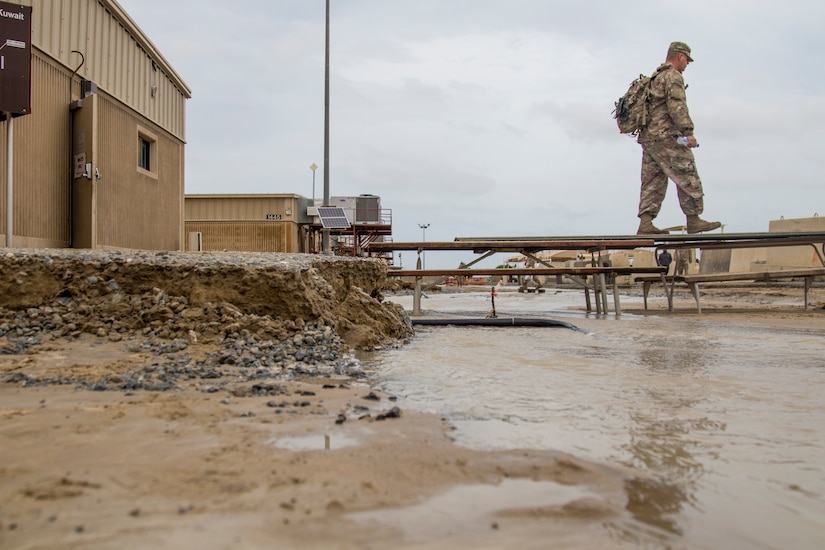 A Soldier walks across a makeshift bridge of picnic tables to avoid  flood waters at Camp Arifjan, Kuwait, November 15, 2018.  The flooding came after an unusually heavy rainstorm hit the area, which has already experienced significant rain this month.