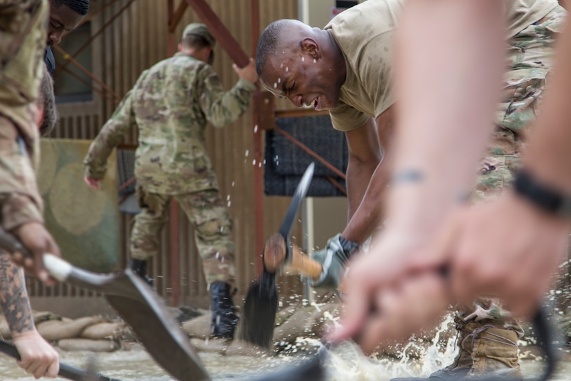 A Soldier uses a pickaxe to dig a trench in order to divert flood waters away from a barracks building at Camp Arifjan, Kuwait, November 15, 2018. Soldiers from multiple units joined together to respond to the flooding in order to protect their living quarters.