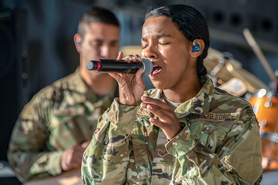 An airman holds a microphone and sings.