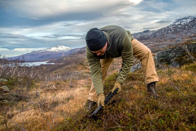 A Marine bends down on hill.
