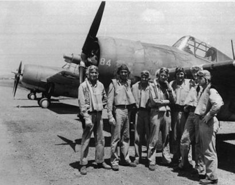 World War II aircrew stands in front of an airplane.