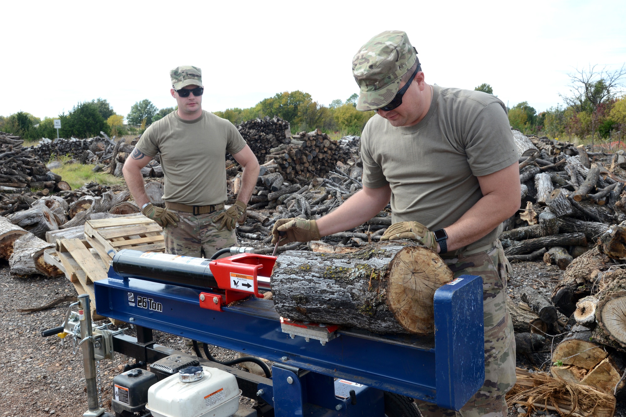 Staff Sgts. Josh Dowding and Eric Gibson, with the 76th Expeditionary Maintenance Squadron, work together to cut large stumps and logs into smaller pieces for firewood.