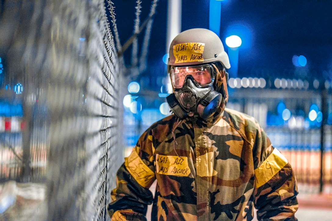 An airman wearing a gas mask walks along a fenced perimeter.