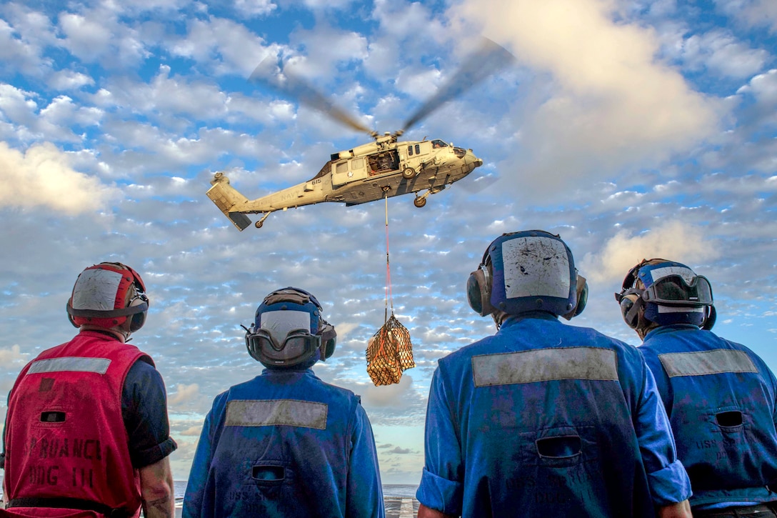 Sailors watch a helicopter carry cargo to where they will retrieve it.