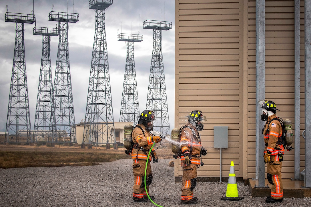 A firefighter sprays another with a hose outside a building.