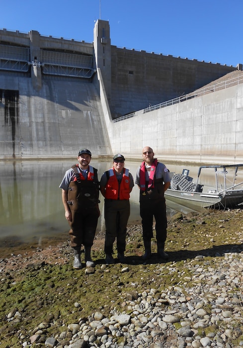 JOHN MARTIN RESERVOIR, Colo. – John Martin park rangers (l-r) Tucker Feyder, Valerie Thompson, and Christopher Gauger stand in front of the electrofishing boat at the bottom of the dam, Nov. 1, 2018. Part of the $6 million stilling basin dewatering project involves the removal of the fish from the stilling basin. Photo by Kim Falen. This was a 2018 photo drive entry.