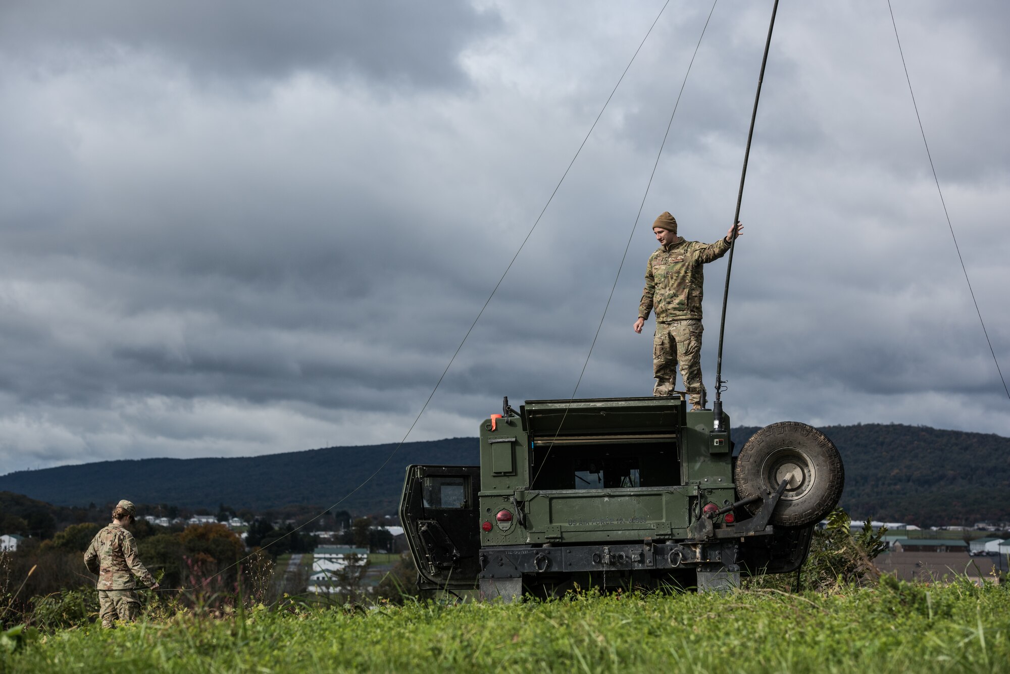 Tech. Sgt. Nathan Belanger holds up a whip antenna while Staff Sgt. Chloe Rangel stakes down the support wires.