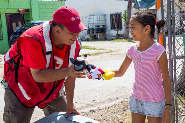 A sergeant hands a young girl a stuffed doll