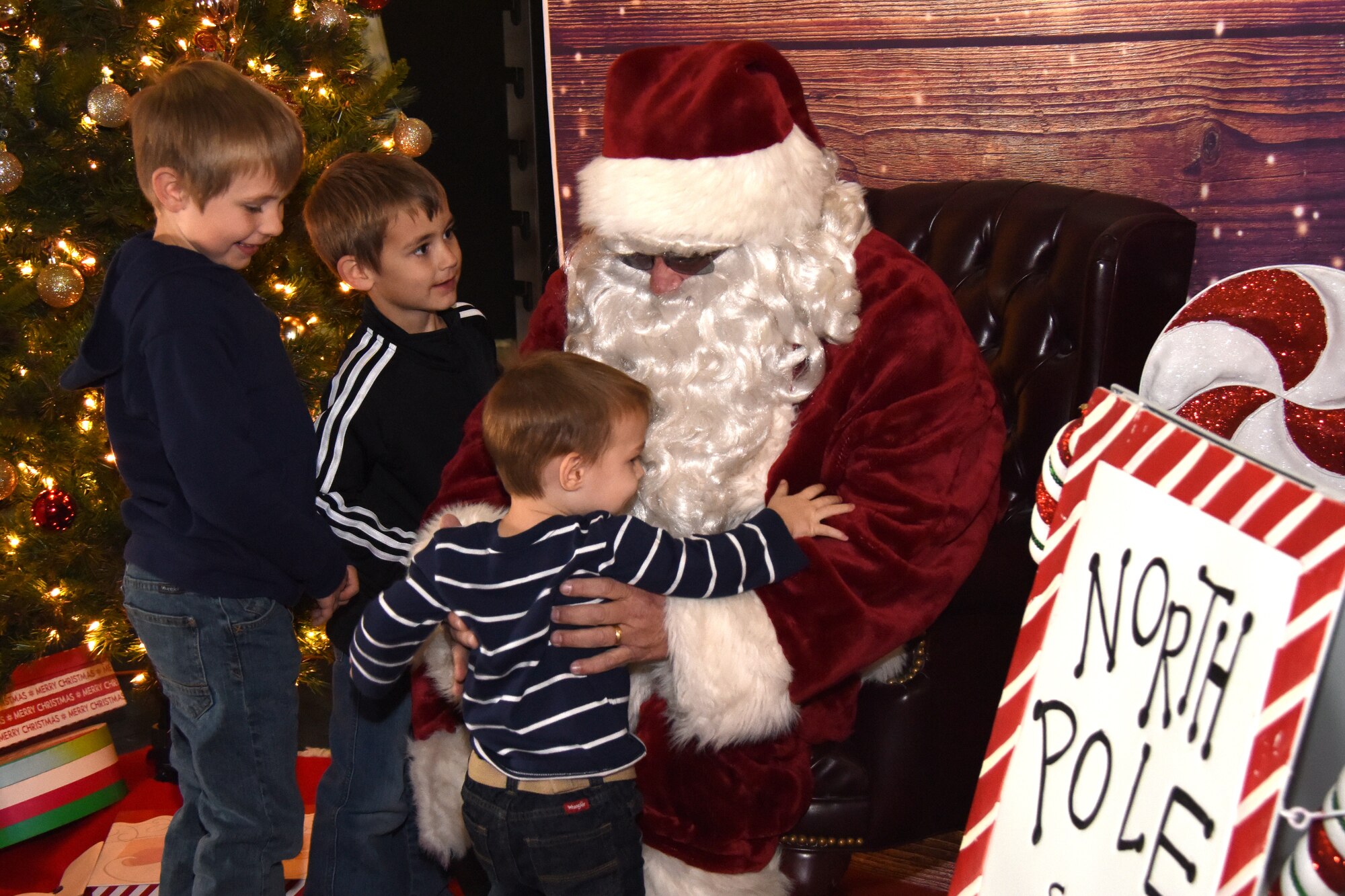 Santa Clause helps a child onto his lap for a photo before listening to requests for presents at the 38th Annual Santa’s Market in the Louis F. Garland Department of Defense Fire Academy on Goodfellow Air Force Base, Texas, Nov. 17, 2018. The children also had a chance to color ornaments and see the Grinch at the event. (U.S. Air Force photo by Airman 1st Class Seraiah Hines/Released)