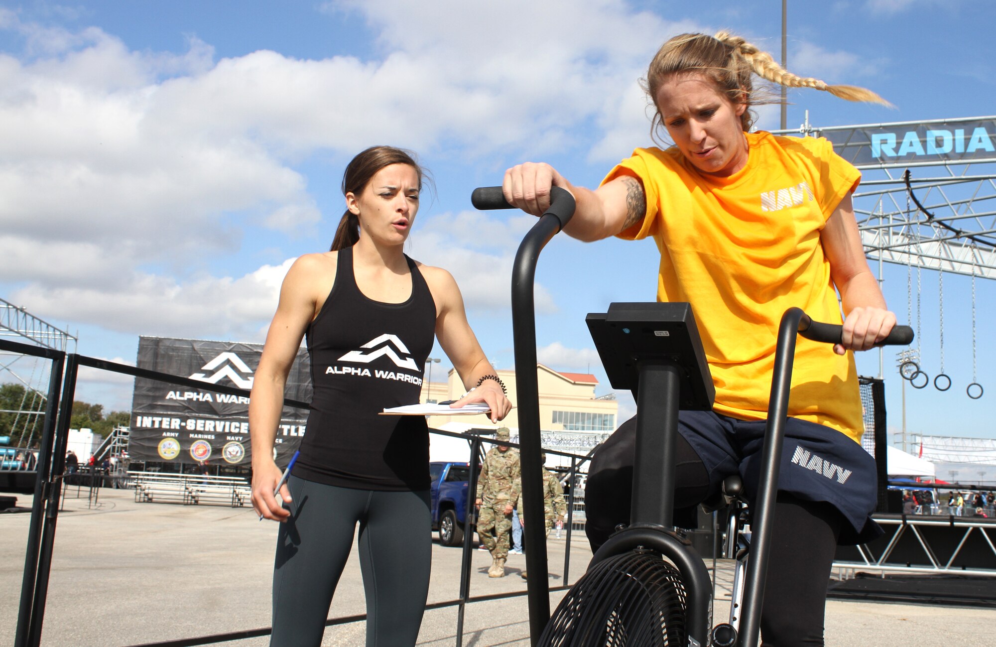 Navy Lt. j.g. Amanda Graham pushes on the bike strength station as Alpha Warrior pro athlete Tawnee Leonardo keeps track of her mileage during the first Inter-service Alpha Warrior Final Battle Nov. 17, 2018, Retama Park, Selma, Texas. (U.S. Air Force photo by Debbie Aragon)