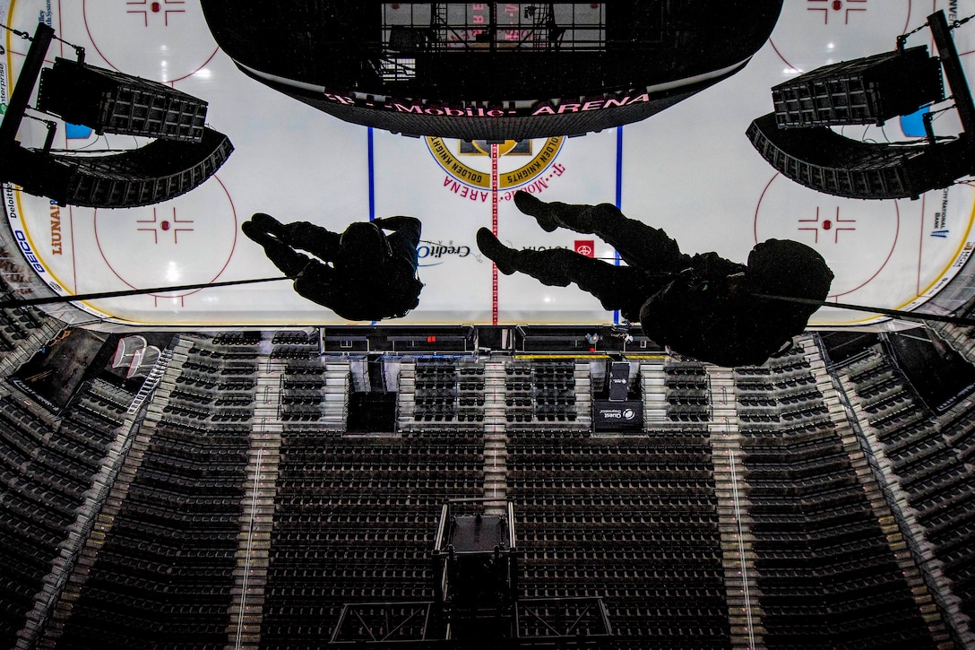 Two airmen rappel  form the rafters of an arena.