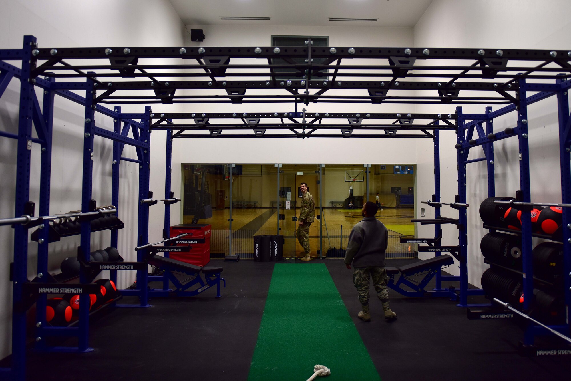 Two men in military uniform stand in a room with workout equipment.