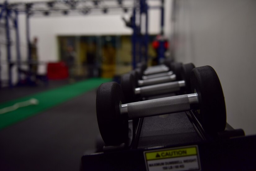 Dumbbells are in focus with workout equipment in the background.