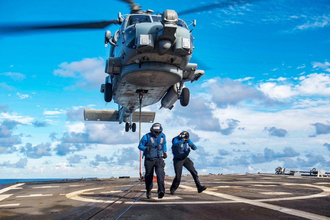 Two sailors run away from a helicopter taking off.