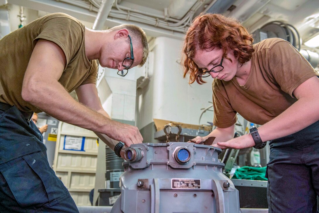 Two sailors work on a piece of hardware.