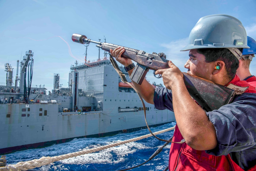 A sailor fires a line shot toward another Navy vessel.