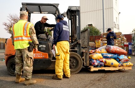 Spc. Mark Maynard, a military police officer with the 870th Military Police Company, and Norm Rosene, public information officer for the North Valley Animal Rescue Group, direct a volunteer moving donations at the municipal airport in Chico, California, Nov. 18, 2018. In response to the Camp Fire, the airport has been converted to a temporary animal shelter, caring for displaced animals and providing donations to pet owners in need.