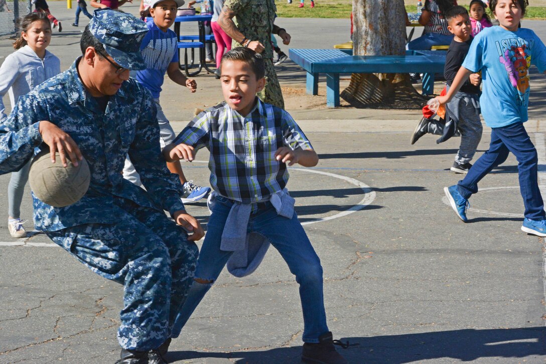 A sailor plays basketball with several students.