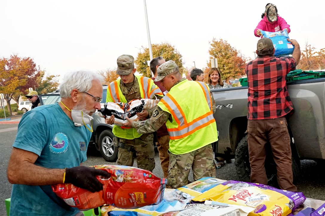 Service members and residents move bags of dog food from the bed of a truck to the pavement.