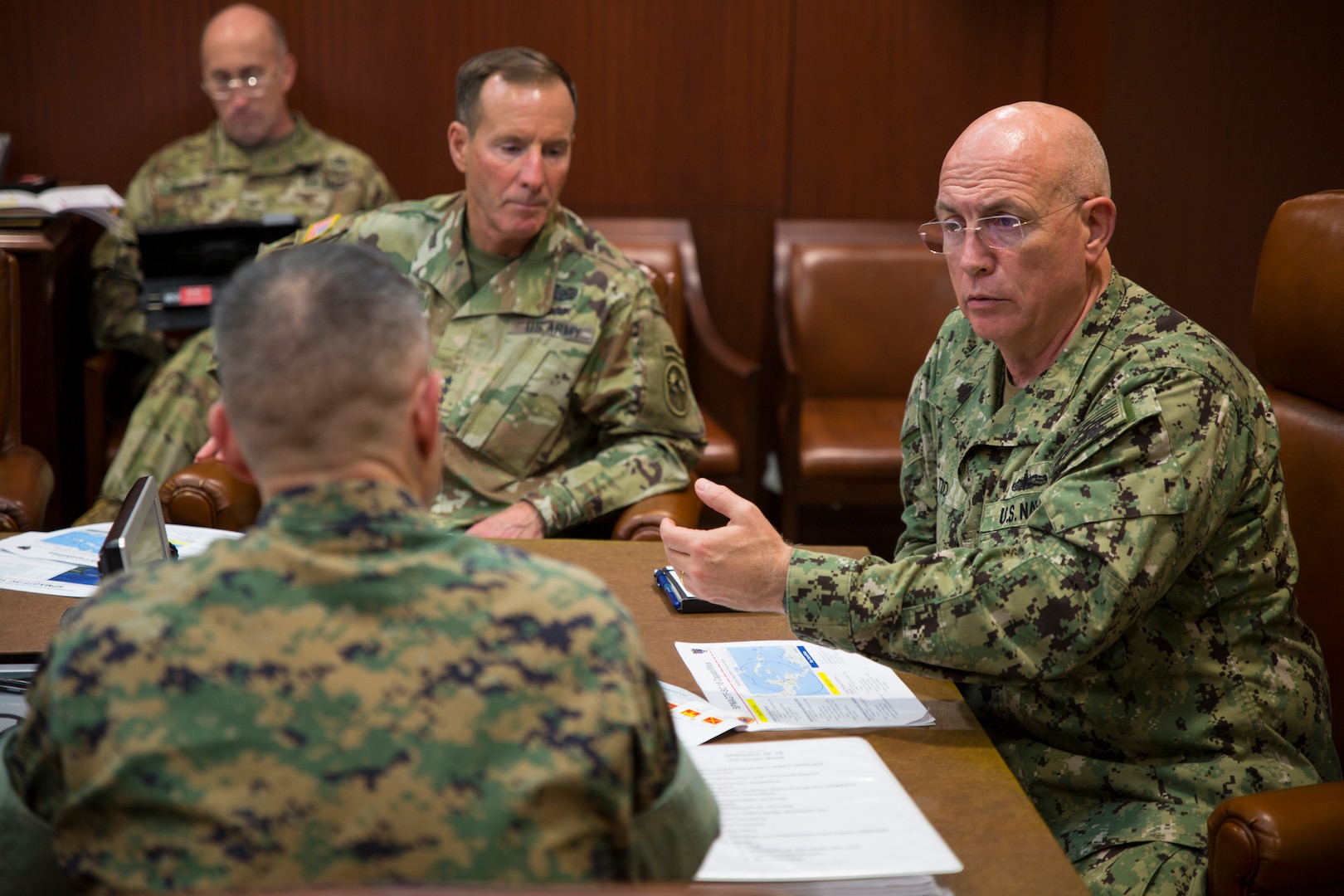 A seated Navy admiral gestures while speaking to a Marine officer.