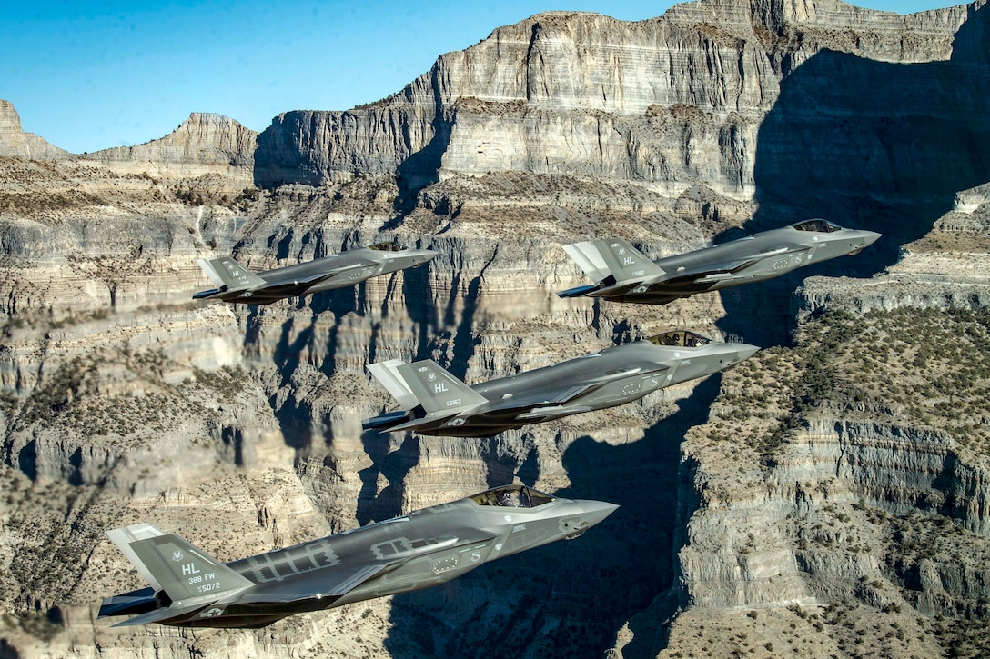 Four Air Force aircraft maneuver near cliffs and mountains.