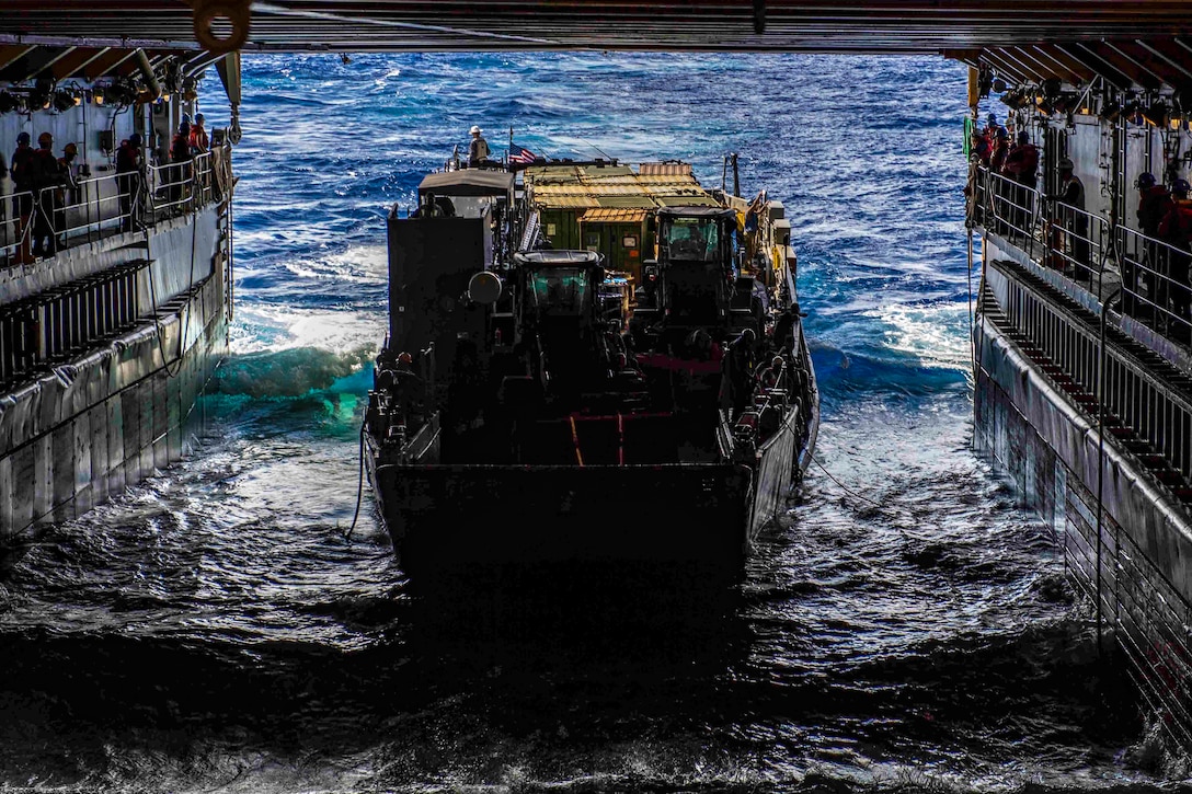 A utility craft enters the well-deck of a large naval vessel.