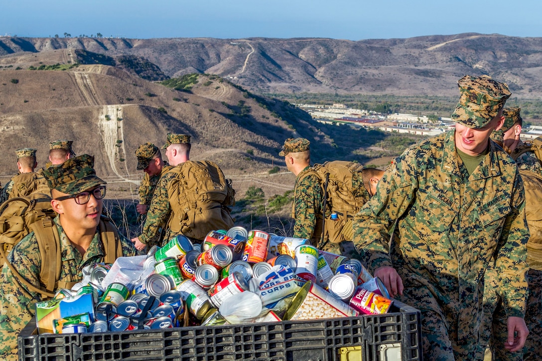 Marines carry a large container of canned food outside.