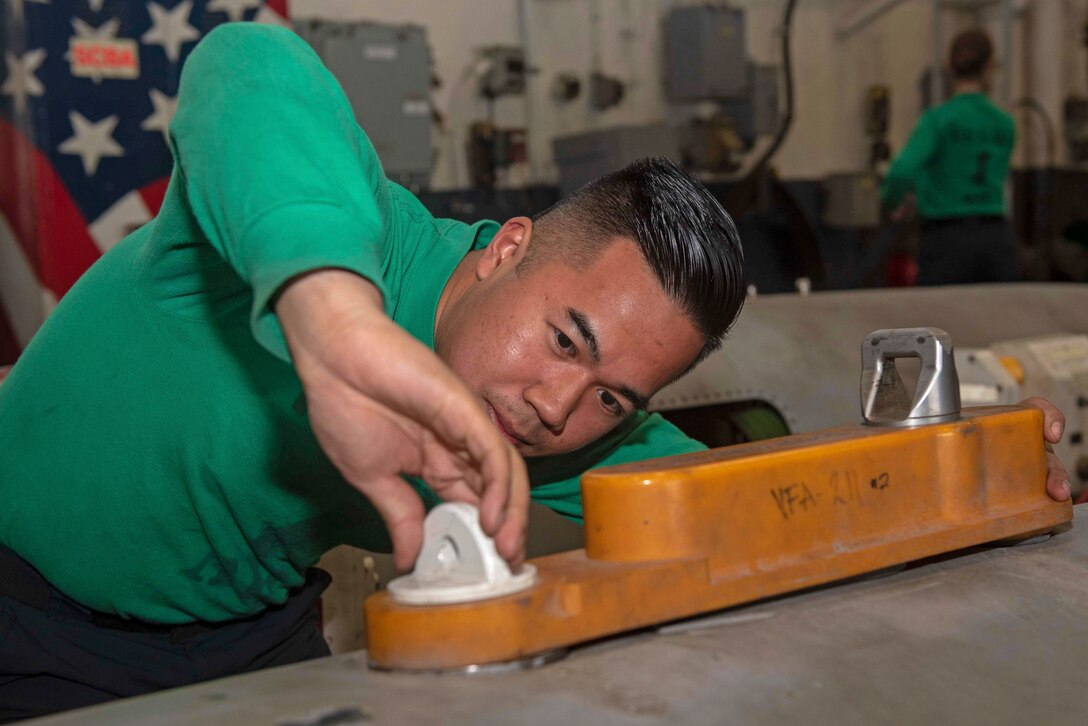 A sailor tightens a part on an aerial refueling storage case.