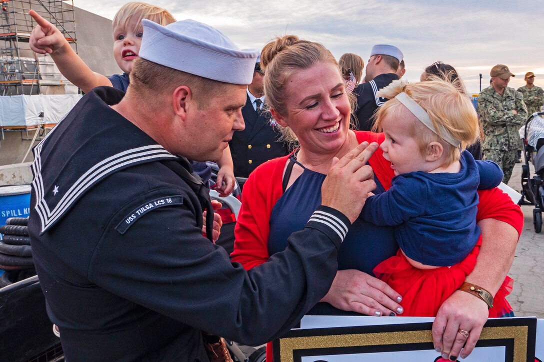 A sailor holding a child interacts with another child being held by a woman.