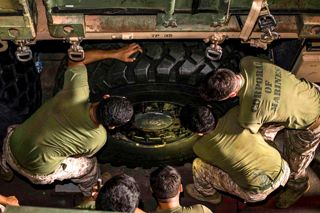 Seven Marines work together to remove a tire from a vehicle.