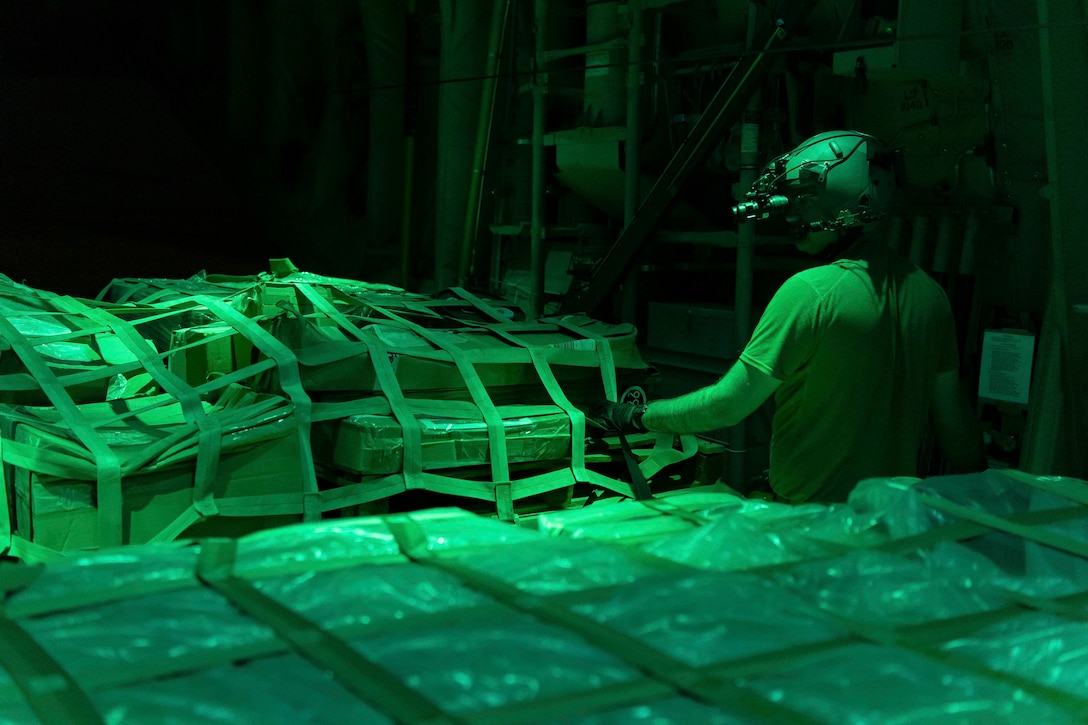 A night vision image shows a man checking over cargo.