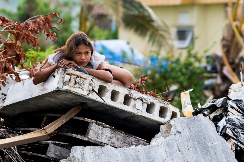 A girl looks on as Guam Air National Guardsmen from the 254th Rapid Engineer Deployable Heavy Operational Repair Squadron Engineers assigned to Andersen Air Force Base build roofing in the village of Koblerville, Saipan, Commonwealth of the Northern Mariana Islands, Nov. 23, 2018, as part of the roof building in support of the Super Typhoon Yutu relief efforts.