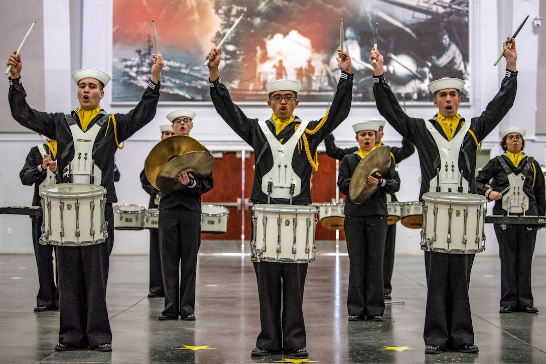 Recruits with drums hold up drumsticks during a performance.