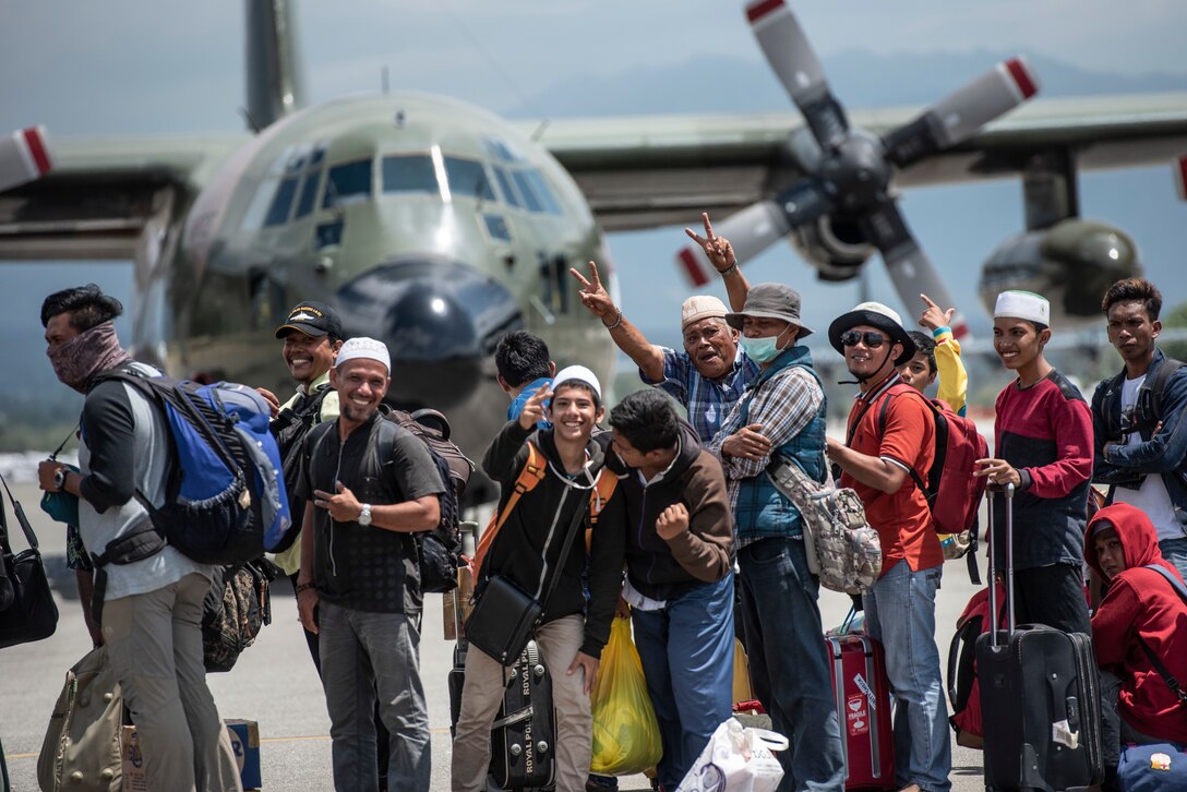 A group of displaced people from Indonesia hold-up a peace sign and say “Thank you America” prior to boarding a U.S. Air Force C-130J Super Hercules in Palu, Indonesia Oct. 10, 2018.