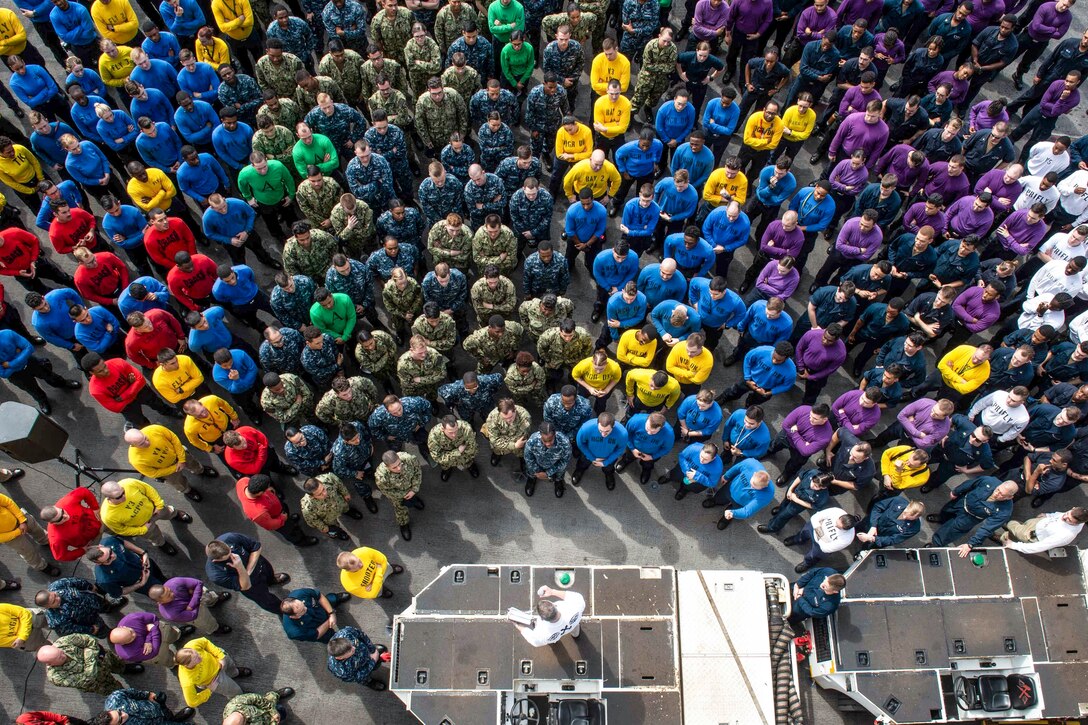 Sailors in different colored shirts, shown from overhead, stand in a group.