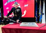 A Marine on a stage prepares to cut a birthday cake on a table