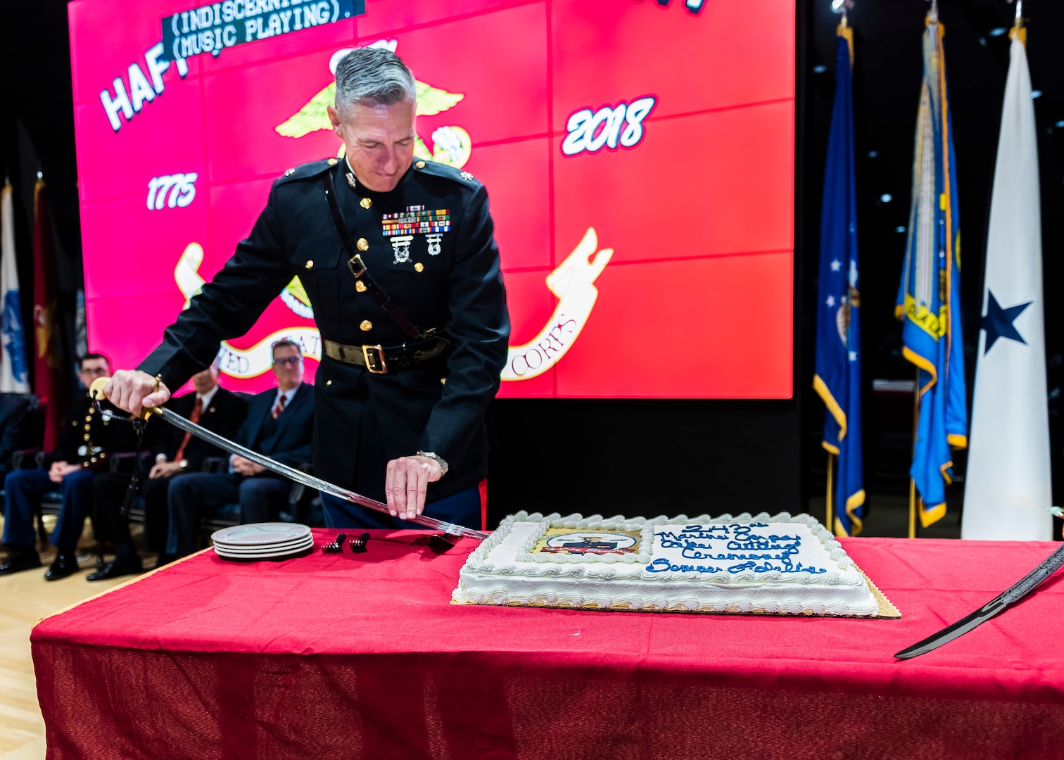 A Marine on a stage prepares to cut a birthday cake on a table