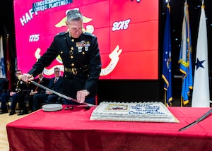 A Marine on a stage prepares to cut a birthday cake on a table