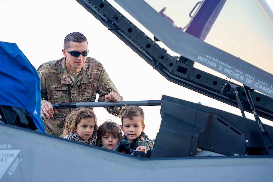 An airman and three children look inside a cockpit.