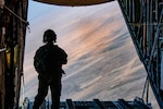 An loadmaster observes a jettisoned load of supplies from the rear of an aircraft in flight.